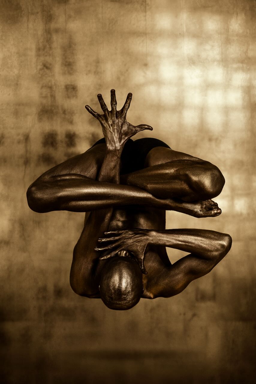 Golden-painted male figure in a dramatic abstract pose with dynamic hand expression, fine art photography by Zack Zublena, suitable for luxury interiors, spas, and modern homes.