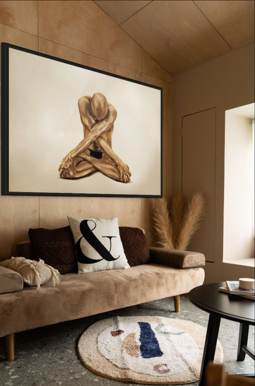 Golden-painted male figure seated cross-legged with arms crossed, displayed as fine art wall decor in a modern living room interior.