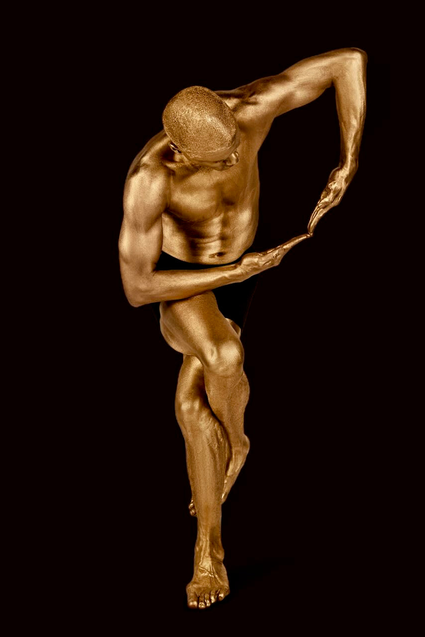 Golden male figure in a sculptural standing pose with arm curved inward – luxury fine art photography for modern interiors, spas, hotels, and collectors.

