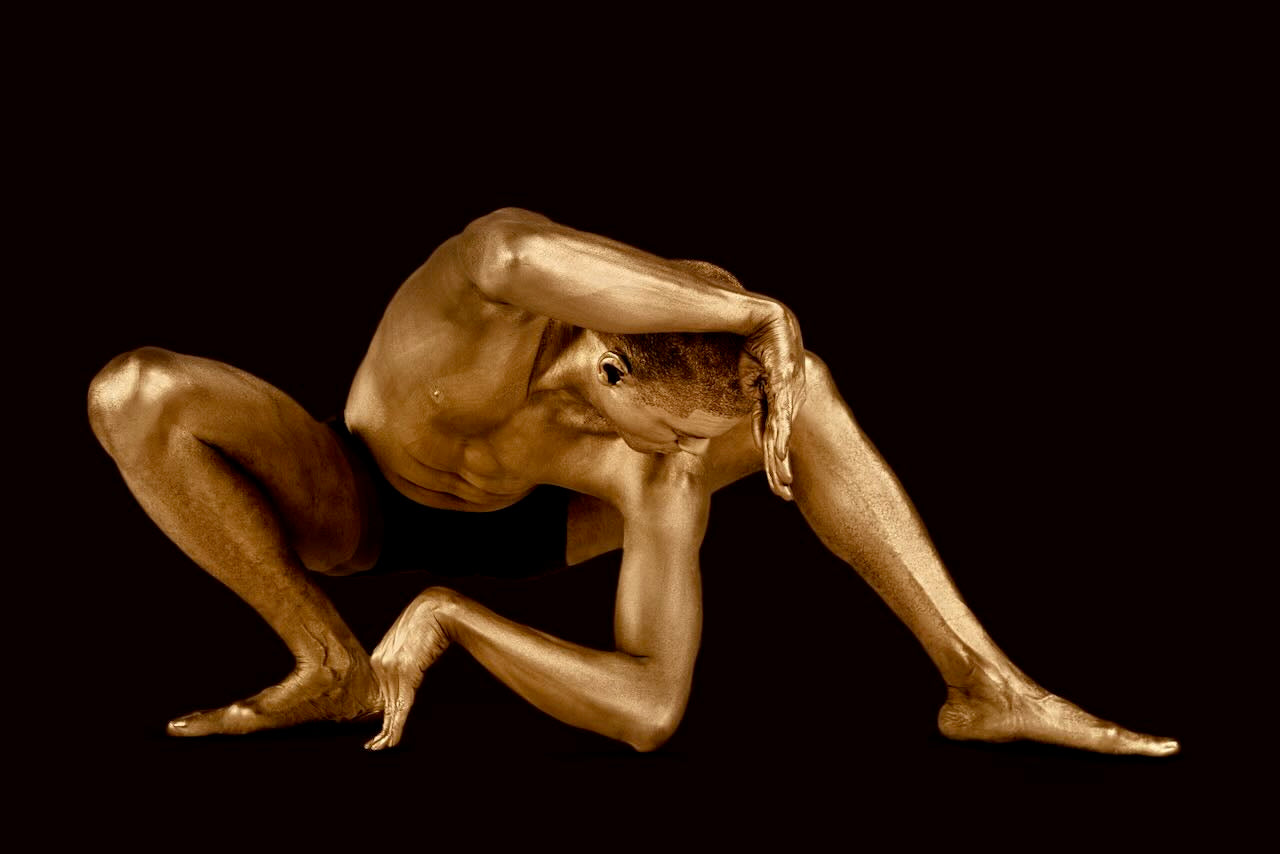 Fine art photograph of a golden-painted male figure in a yoga pose on a dark background, symbolizing balance, focus, and meditation. Ideal wall art print for yoga studios, wellness spaces, and contemporary interiors.
