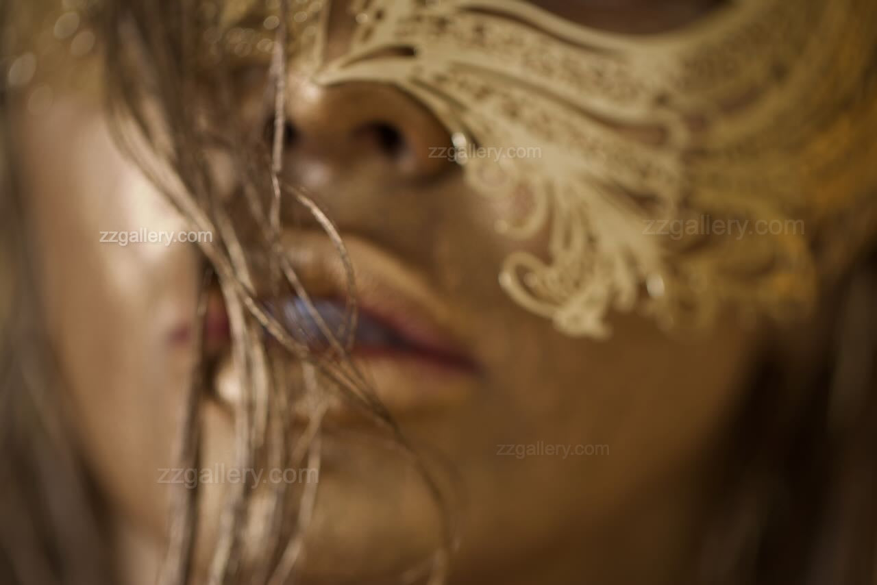 Close-up portrait of a face painted in shimmering gold wearing an ornate golden mask, fine art photography emphasizing sensuality and mystery.