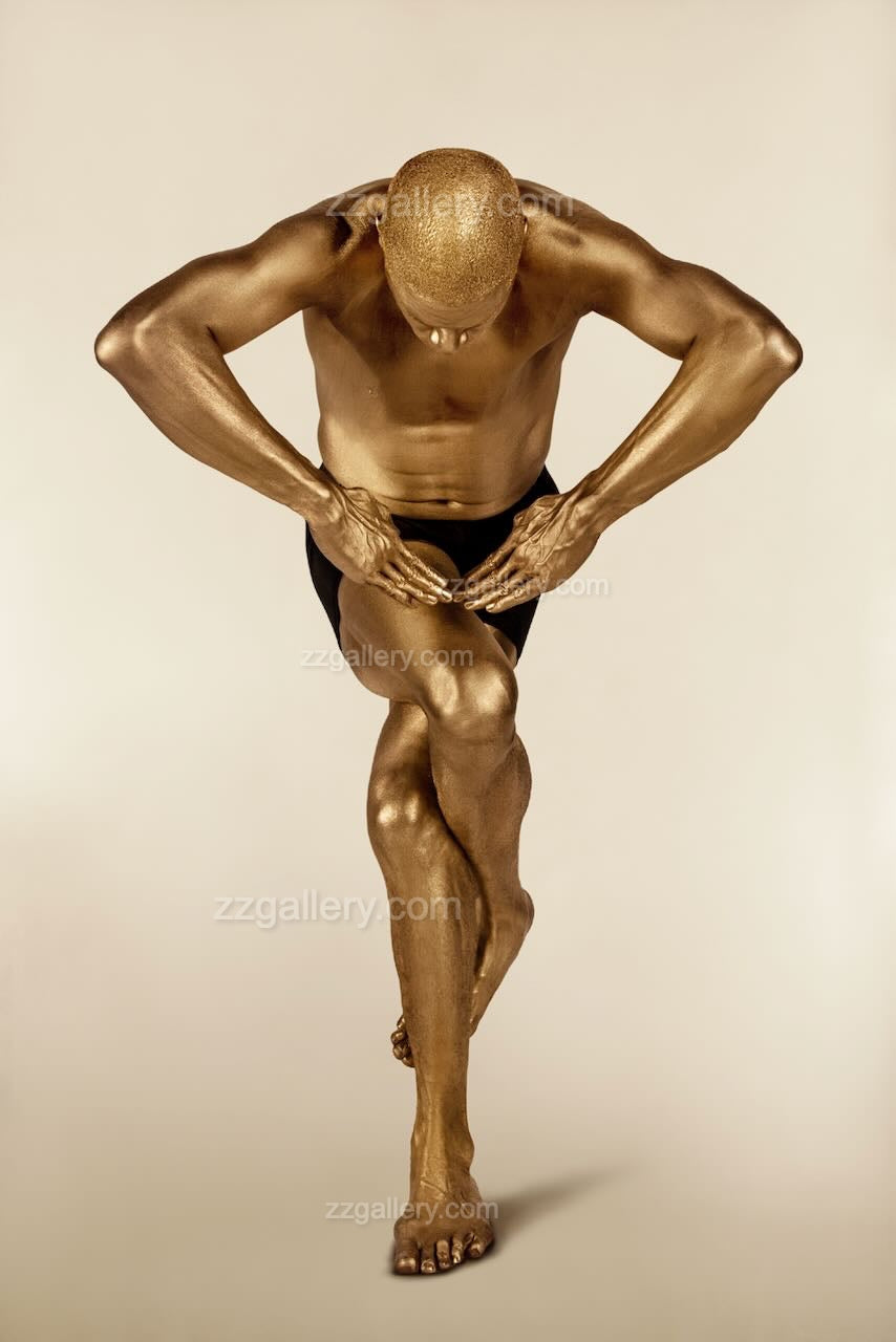 Fine art image of a golden-painted male in a dynamic side bend with sculptural hand framing, blending yoga posture with abstract contemporary wall art for luxury interiors.