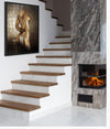 Golden-painted nude female figure with silver tones, viewed from the back, displayed as luxury wall art in a modern staircase interior with marble and fireplace.