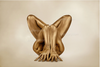 Gold-painted nude body folded in yoga lotus pose against beige background
