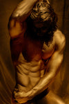 Golden nude male figure in shadowed lighting with sculptural physique, hand over head and torso, evoking sacred masculinity, reverence, and classical grace.