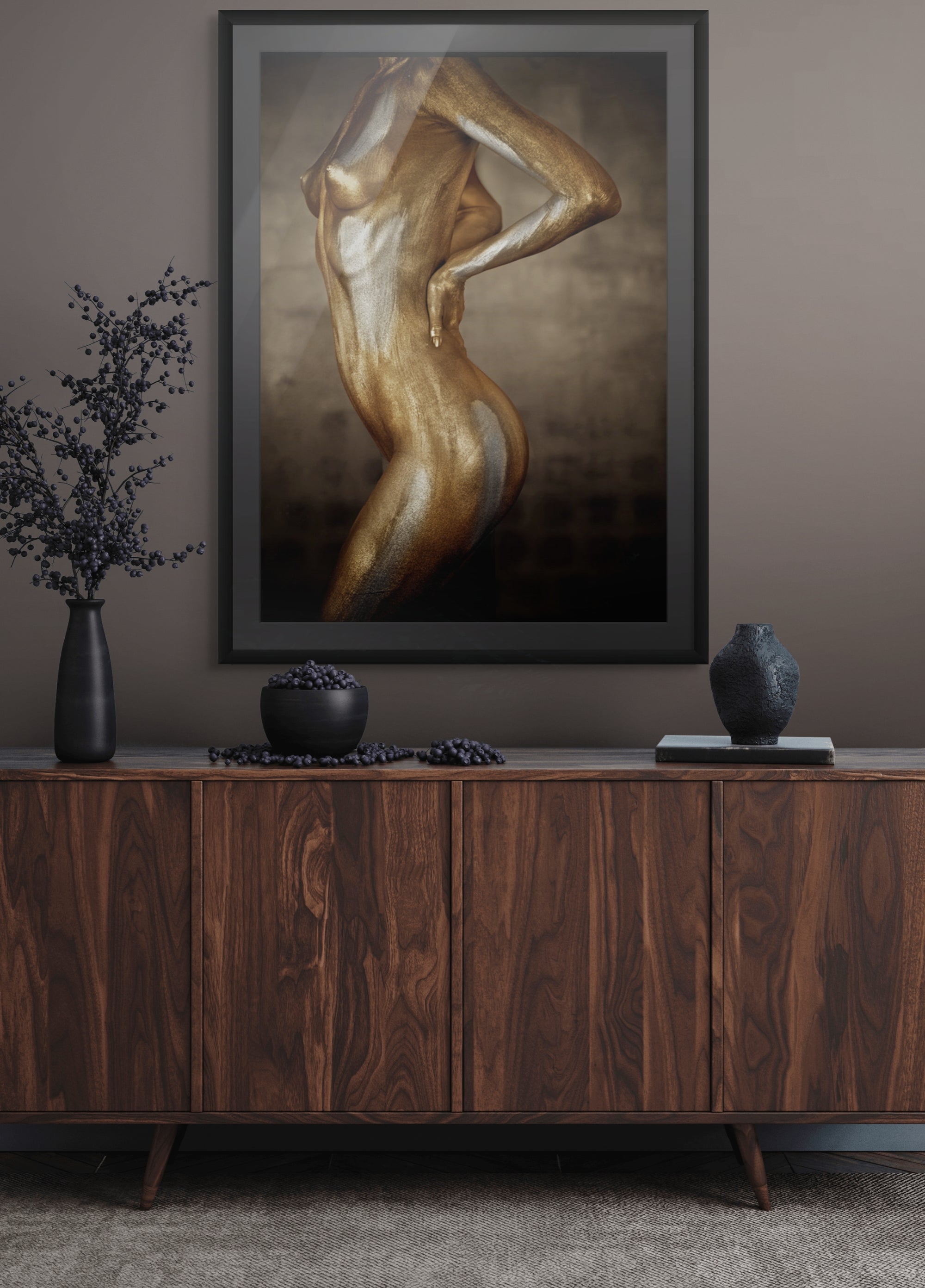 Golden and silver-painted figure in a sculptural pose, luxury fine art wall decor displayed in an elegant modern interior with wooden cabinet and dark ceramic accents.
