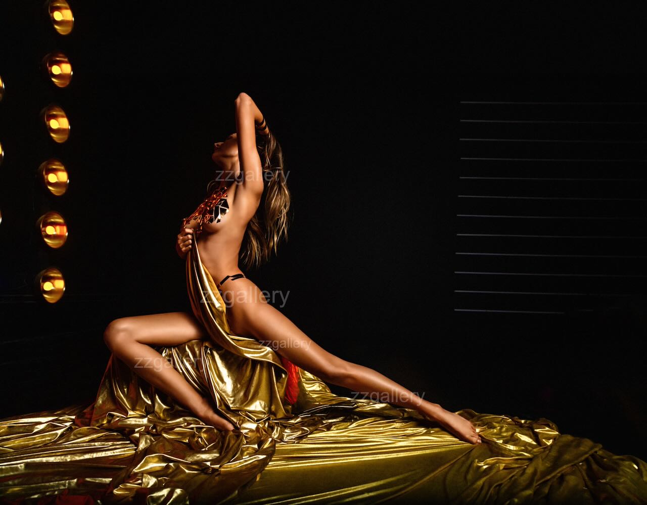 Golden-painted cabaret dancer in an expressive stage pose, draped in shimmering gold fabric with dramatic lighting, symbolizing strength, elegance, and artistic transformation in fine art photography.