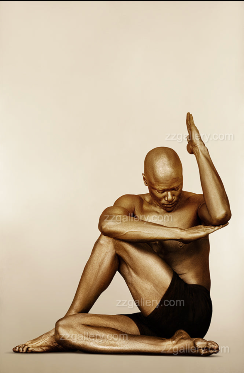Golden-painted yogi in a seated twist with lifted hand and bowed head – spiritual fine art wall photography for wellness and meditation spaces.