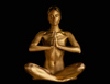 Gold-painted nude woman sitting cross-legged in meditation with prayer hands, fine art photography symbolizing sacred feminine energy and inner peace