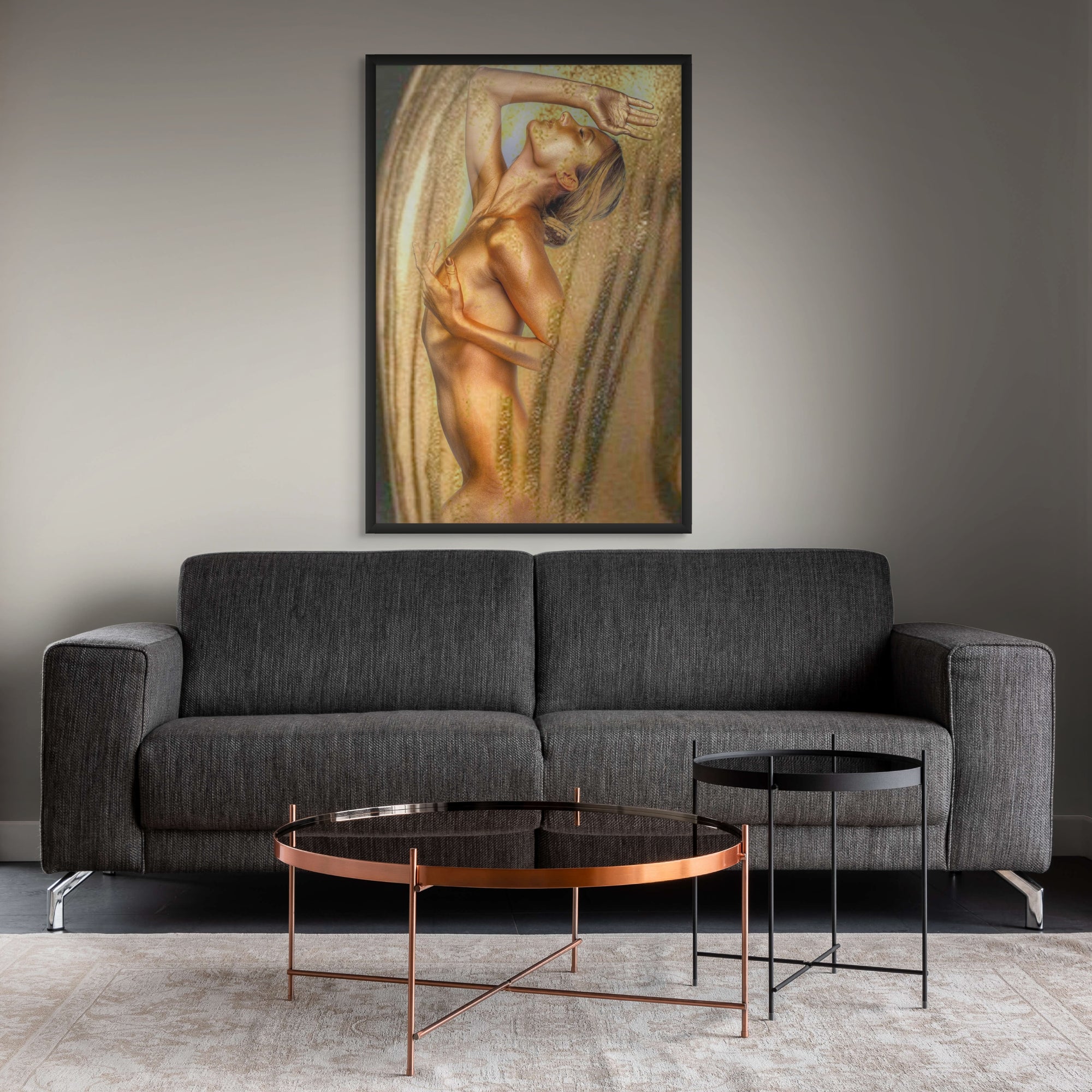 Golden nude female wall art framed in black, hanging above a grey sofa in a stylish modern living room with copper and black tables.