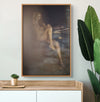 Dreamlike fine art print from the Muse’s Whisper series, showing a golden-painted nude woman in soft focus, blending body and shadow in a reflective composition, styled above a wooden console with modern greenery.