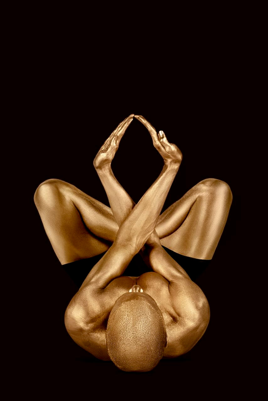 Golden figure lying in sacred diamond mudra pose on black background, fine art photo.