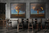 Diptych display of two framed fine art photographs from the Skyfall Flames VI – Phoenix Ascent series, featuring a gold-painted woman with fire in a desert setting, showcased in a modern dining interior.