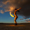 Fine art photograph of a gold-painted woman performing with fire in a desert under dramatic skies, symbolizing phoenix ascent and transformation.