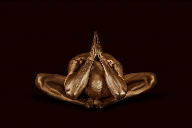 Golden-painted male figure in a deep meditative yoga pose with hands pressed together, fine art photography symbolizing serenity, balance, and strength.