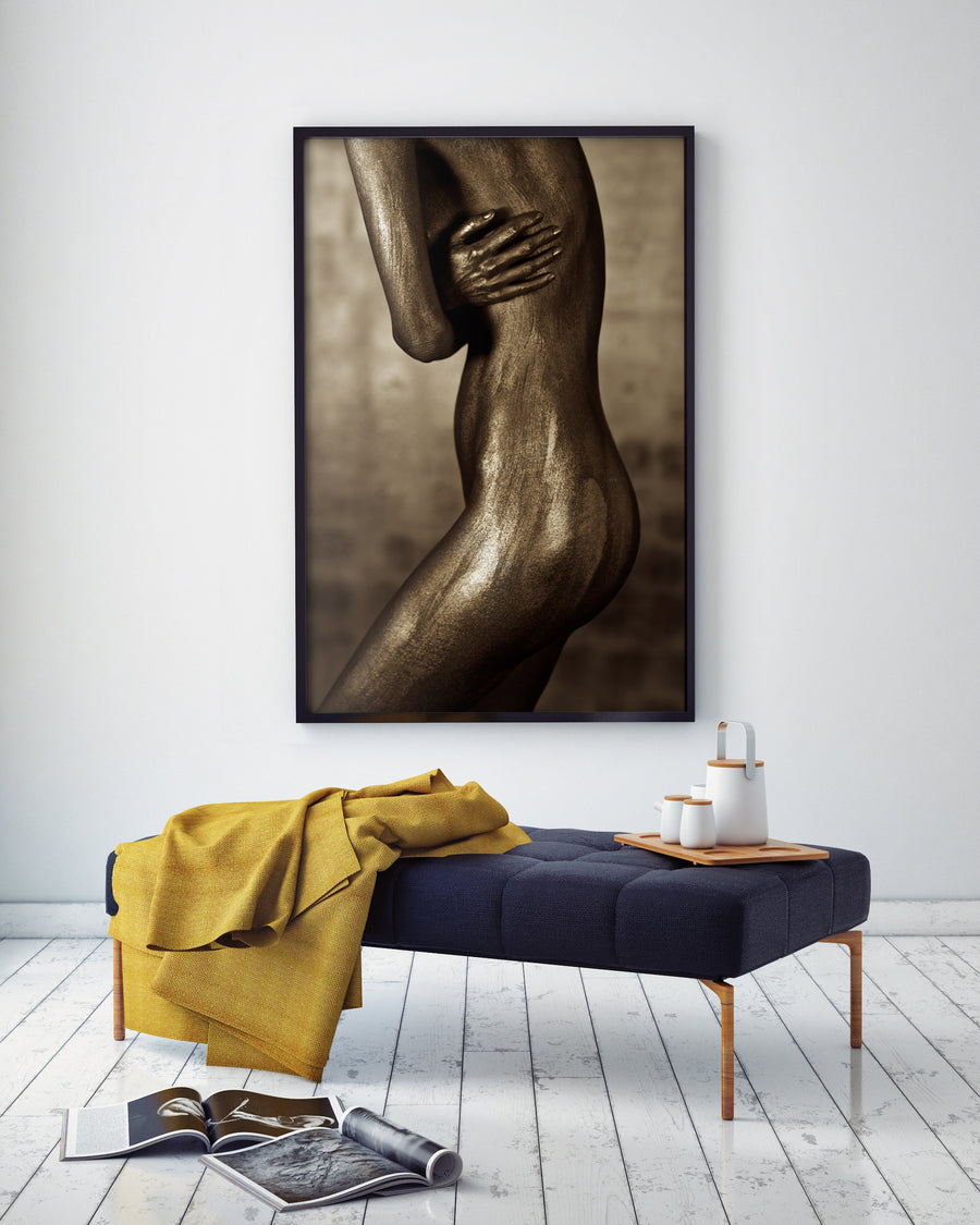 Golden-painted nude female figure shielding her torso with arm and hand, fine art photography symbolizing strength, intimacy, and sacred femininity.